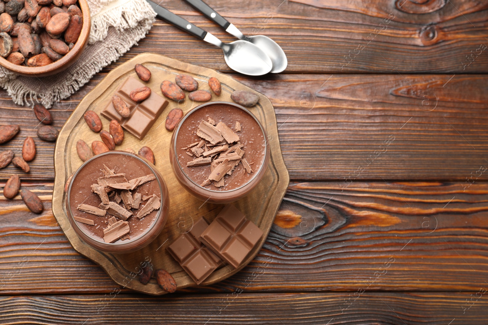 Photo of Delicious chocolate panna cotta in glasses, cocoa beans and chocolate pieces on wooden table, flat lay. Space for text