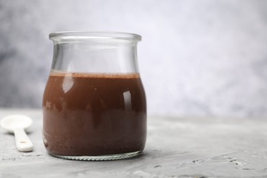 Photo of Delicious panna cotta in glass jar on grey textured table, closeup. Space for text