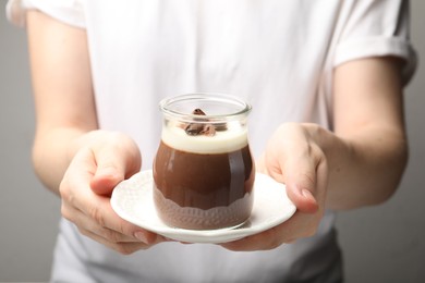 Photo of Woman holding glass jar with delicious panna cotta against grey background, closeup