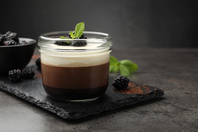 Photo of Tasty panna cotta with blackberries and mint in jar at grey table, closeup. Space for text
