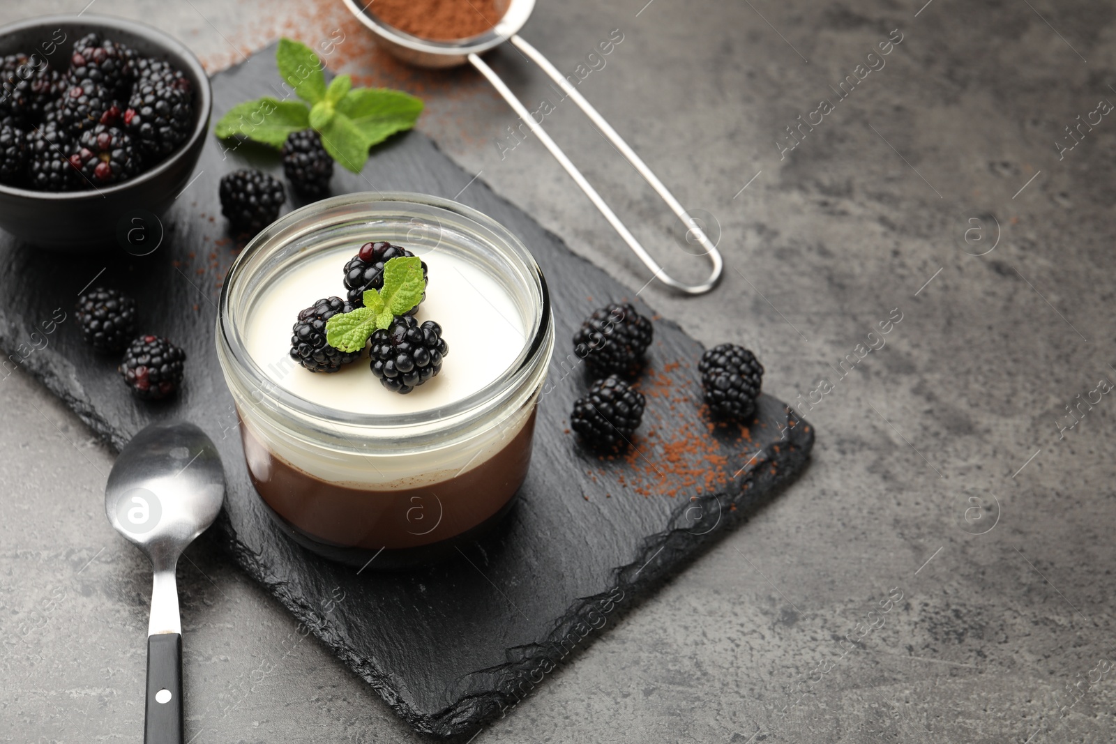 Photo of Tasty panna cotta with blackberries, mint and cocoa powder on grey table. Space for text