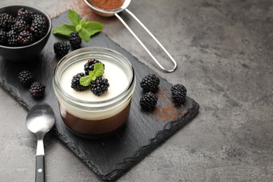 Photo of Tasty panna cotta with blackberries, mint and cocoa powder on grey table. Space for text