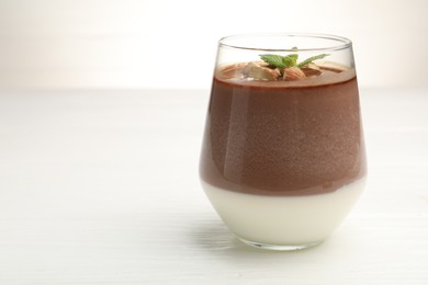 Photo of Delicious chocolate panna cotta with almonds and mint in glass on white table, closeup. Space for text