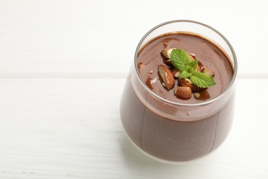 Photo of Delicious chocolate panna cotta with almonds and mint in glass on white table, closeup. Space for text