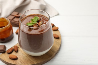 Photo of Delicious chocolate panna cotta with almonds, mint and caramel sauce on white wooden table, closeup. Space for text