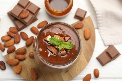 Photo of Delicious chocolate panna cotta with almonds, mint and caramel sauce on white wooden table, flat lay