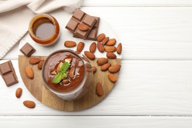 Photo of Delicious chocolate panna cotta with almonds, mint and caramel sauce on white wooden table, flat lay. Space for text