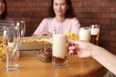 Photo of Group of friends with beer and snacks having fun at wooden table indoors, selective focus