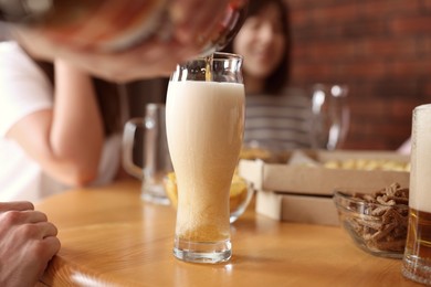 Photo of Woman pouring beer into glass at wooden table indoors, selective focus