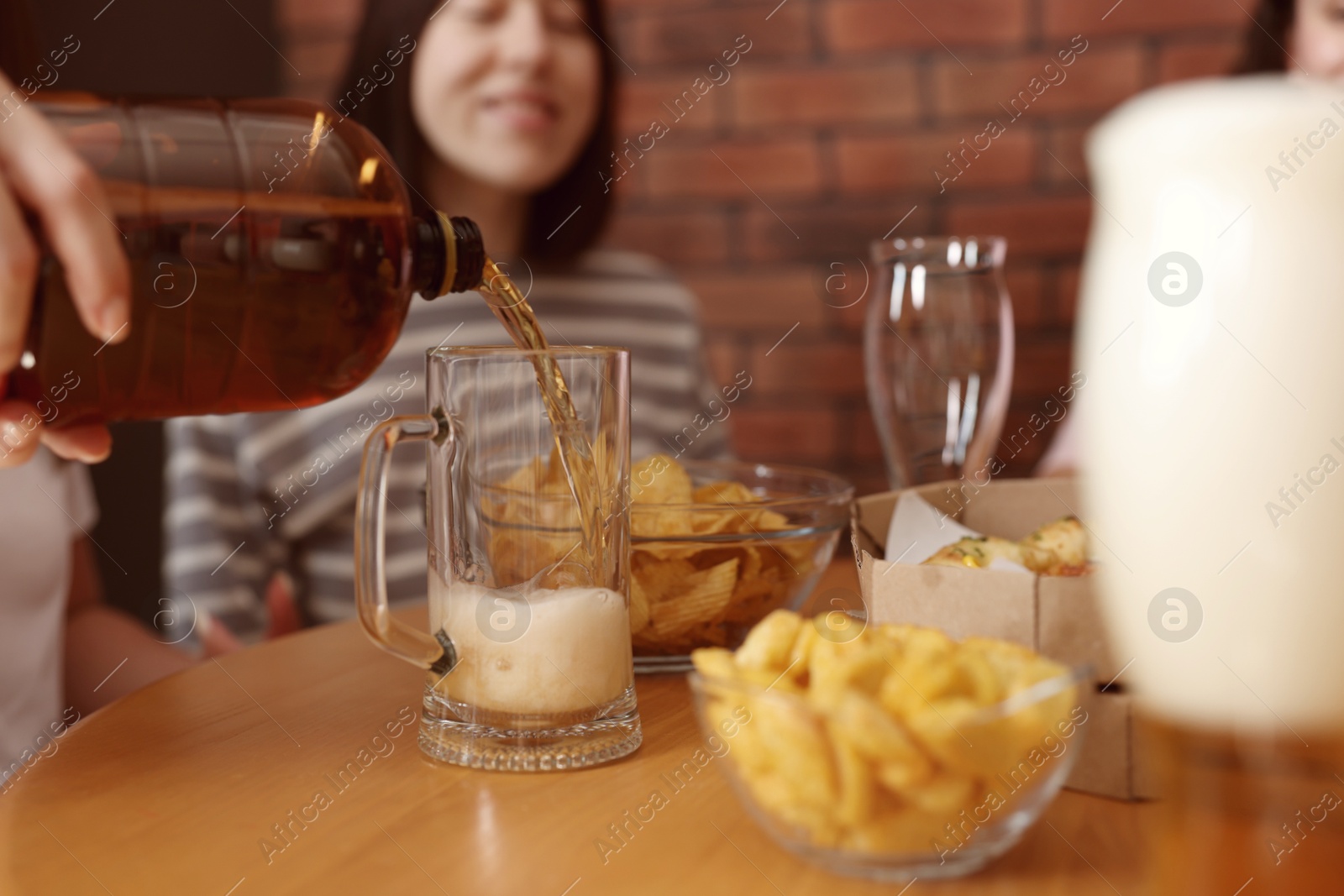Photo of Woman pouring beer into glass at wooden table indoors, selective focus