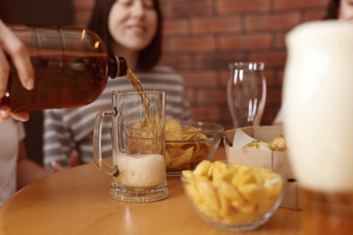 Photo of Woman pouring beer into glass at wooden table indoors, selective focus