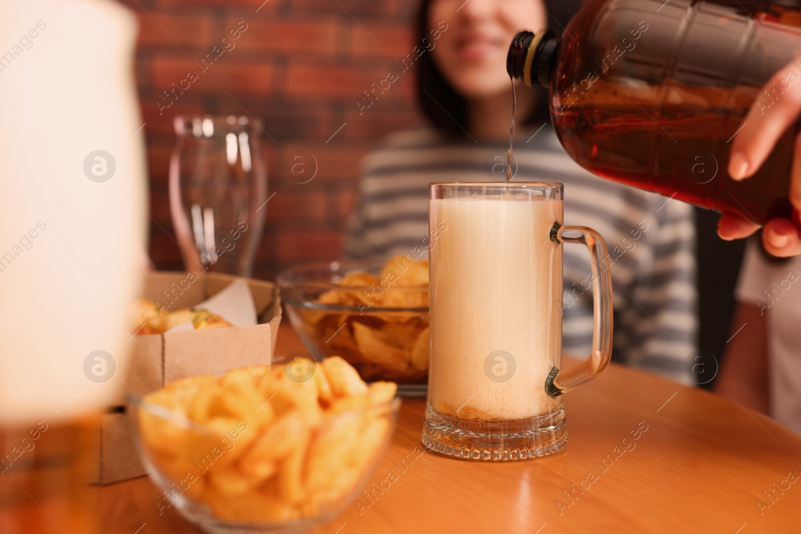 Photo of Woman pouring beer into glass at wooden table indoors, selective focus