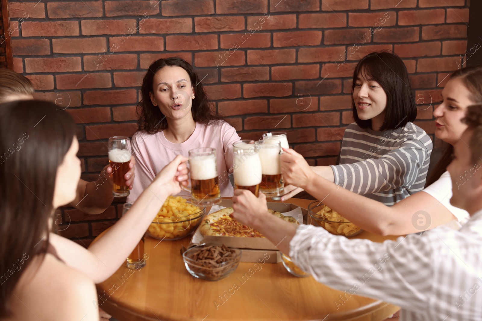 Photo of Group of happy friends clinking glasses of beer at table with food indoors