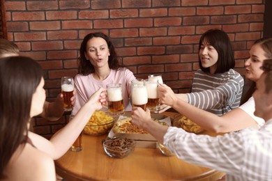 Photo of Group of happy friends clinking glasses of beer at table with food indoors