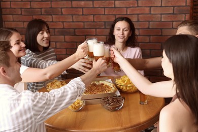 Photo of Group of happy friends clinking glasses of beer at table with food indoors