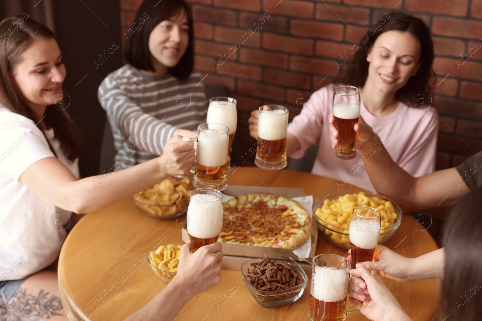 Photo of Group of happy friends clinking glasses of beer at table with food indoors, selective focus