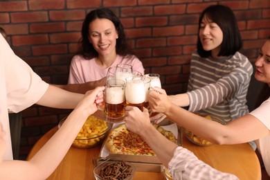 Photo of Group of happy friends clinking glasses of beer at table with food indoors, selective focus