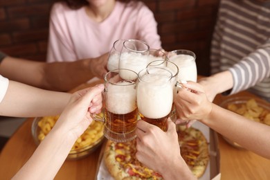 Photo of Group of friends clinking glasses of beer at table indoors, closeup