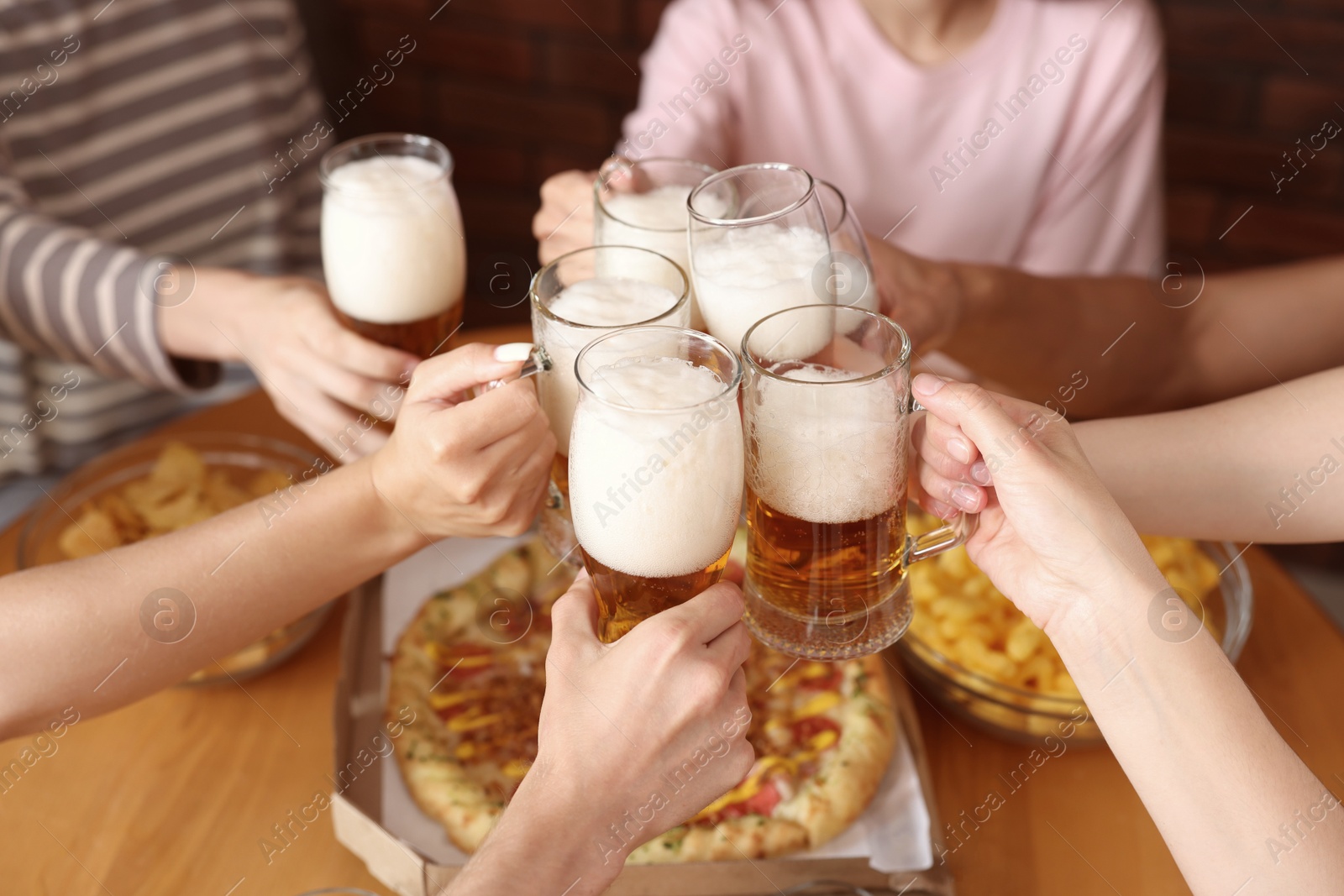 Photo of Group of friends clinking glasses of beer at table indoors, closeup