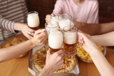 Photo of Group of friends clinking glasses of beer at table indoors, closeup