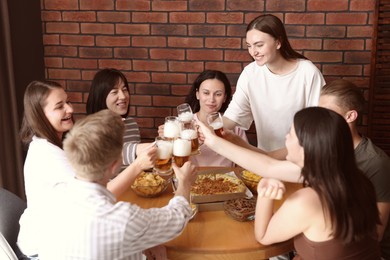 Photo of Group of happy friends clinking glasses of beer at table with food indoors