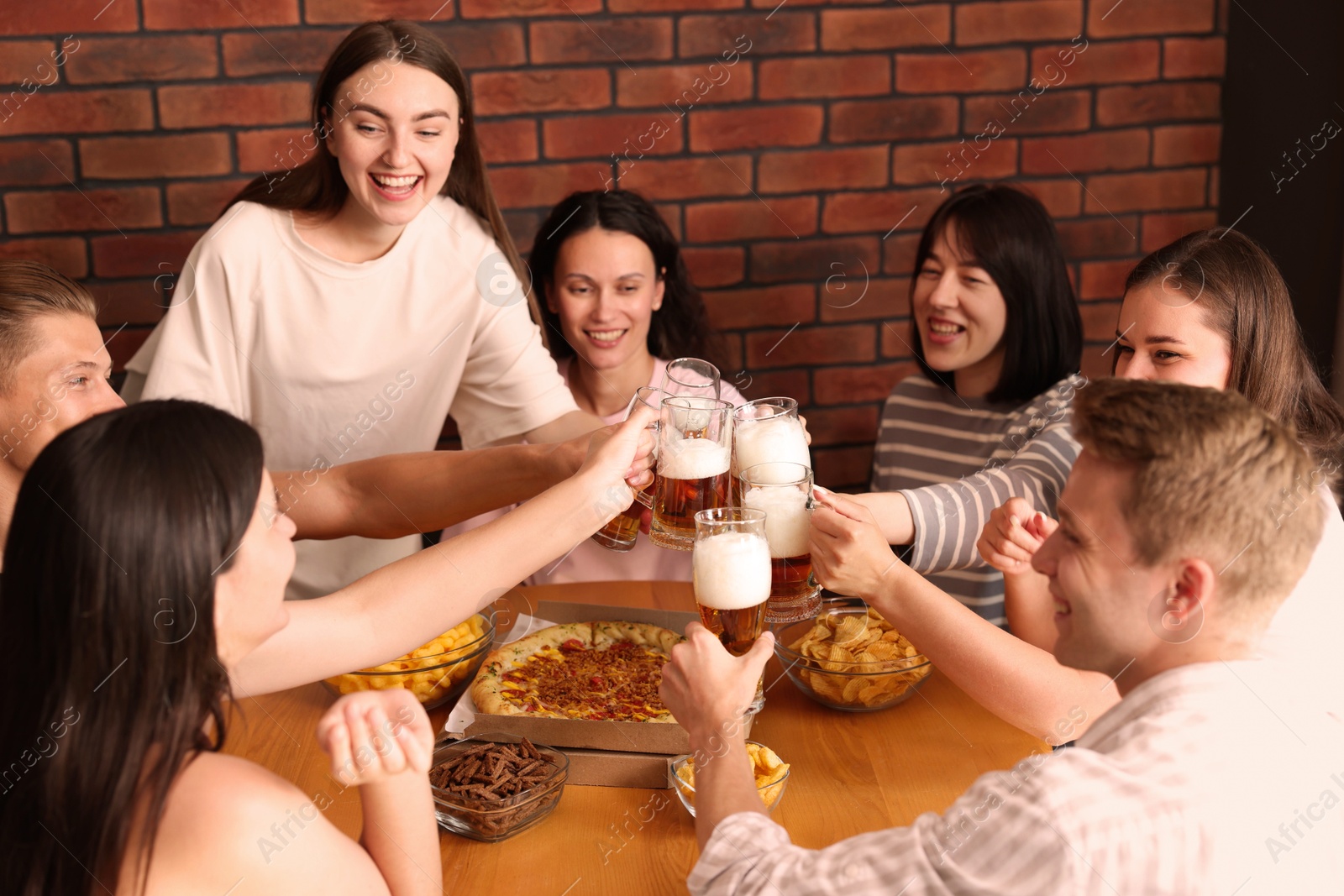 Photo of Group of happy friends clinking glasses of beer at table with food indoors