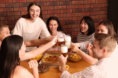 Photo of Group of happy friends clinking glasses of beer at table with food indoors