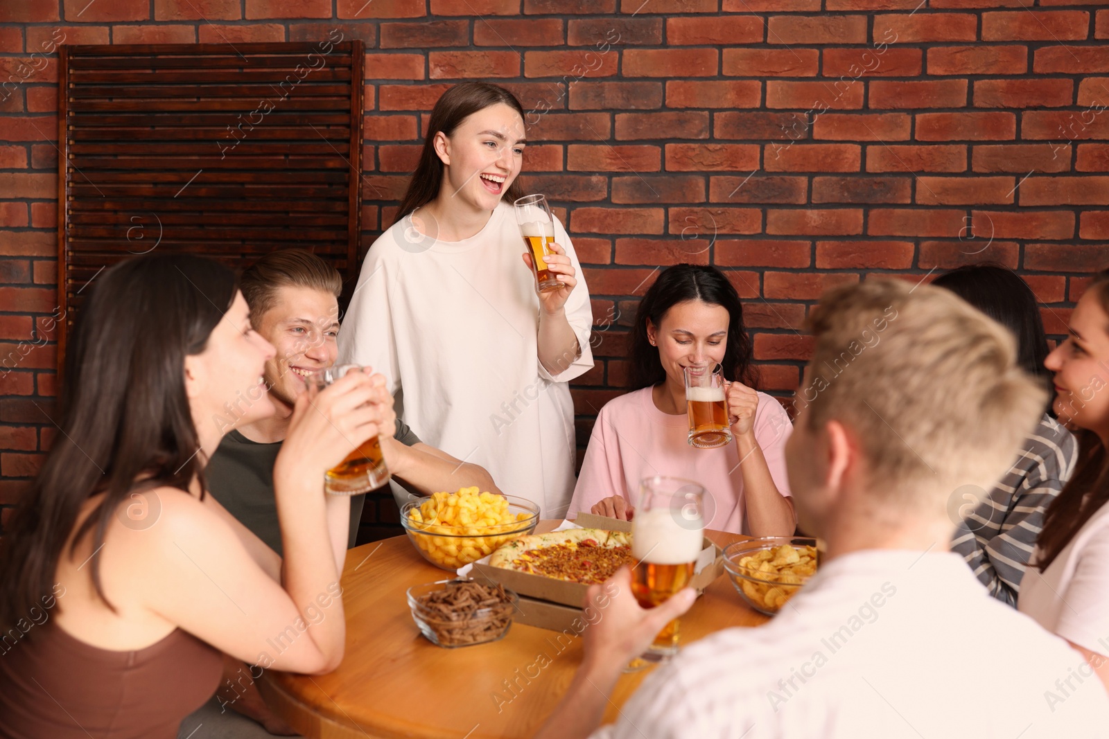 Photo of Group of friends with beer and snacks having fun at wooden table indoors