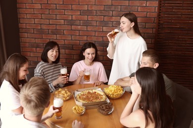 Photo of Group of friends with beer and snacks having fun at wooden table indoors