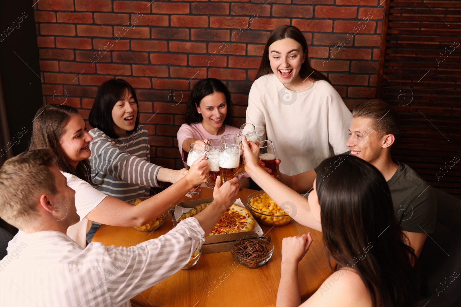 Photo of Group of happy friends clinking glasses of beer at table indoors