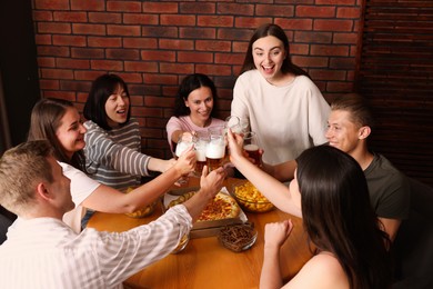 Photo of Group of happy friends clinking glasses of beer at table indoors