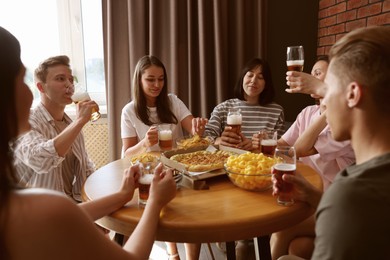 Photo of Group of friends with beer and snacks having fun at wooden table indoors
