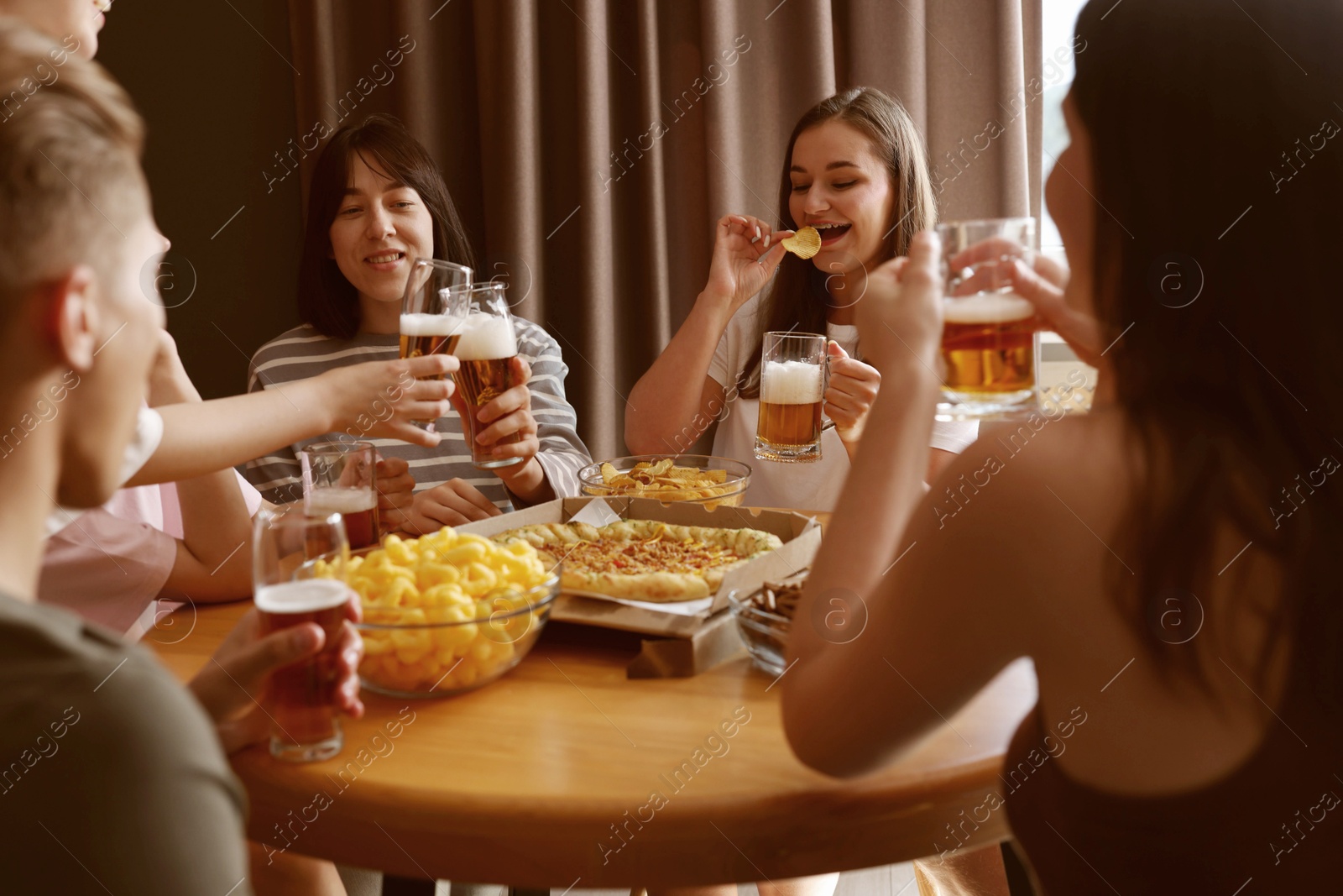 Photo of Group of friends with beer and snacks having fun at wooden table indoors