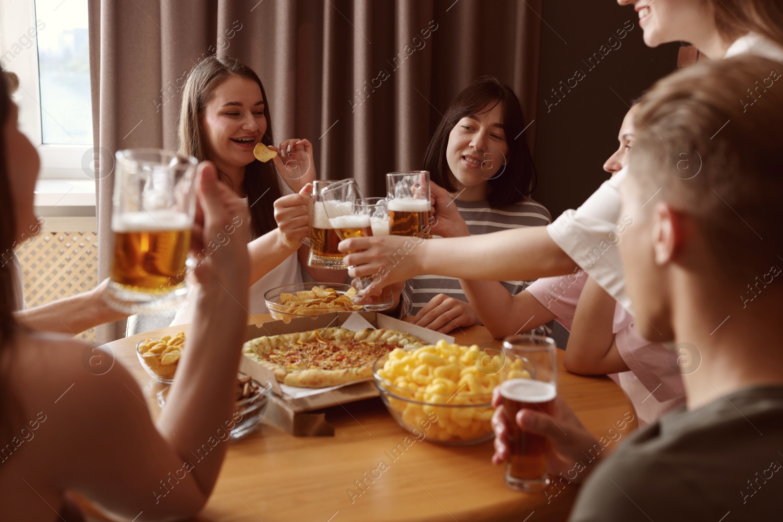 Photo of Group of happy friends clinking glasses of beer at table indoors