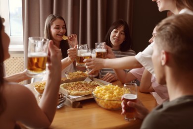 Photo of Group of happy friends clinking glasses of beer at table indoors