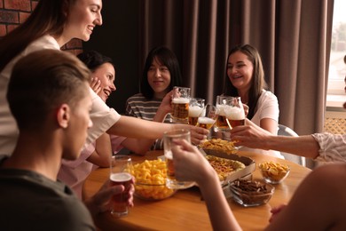 Photo of Group of happy friends clinking glasses of beer at table indoors