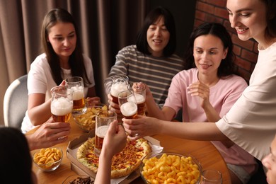Photo of Group of happy friends clinking glasses of beer at table indoors, selective focus