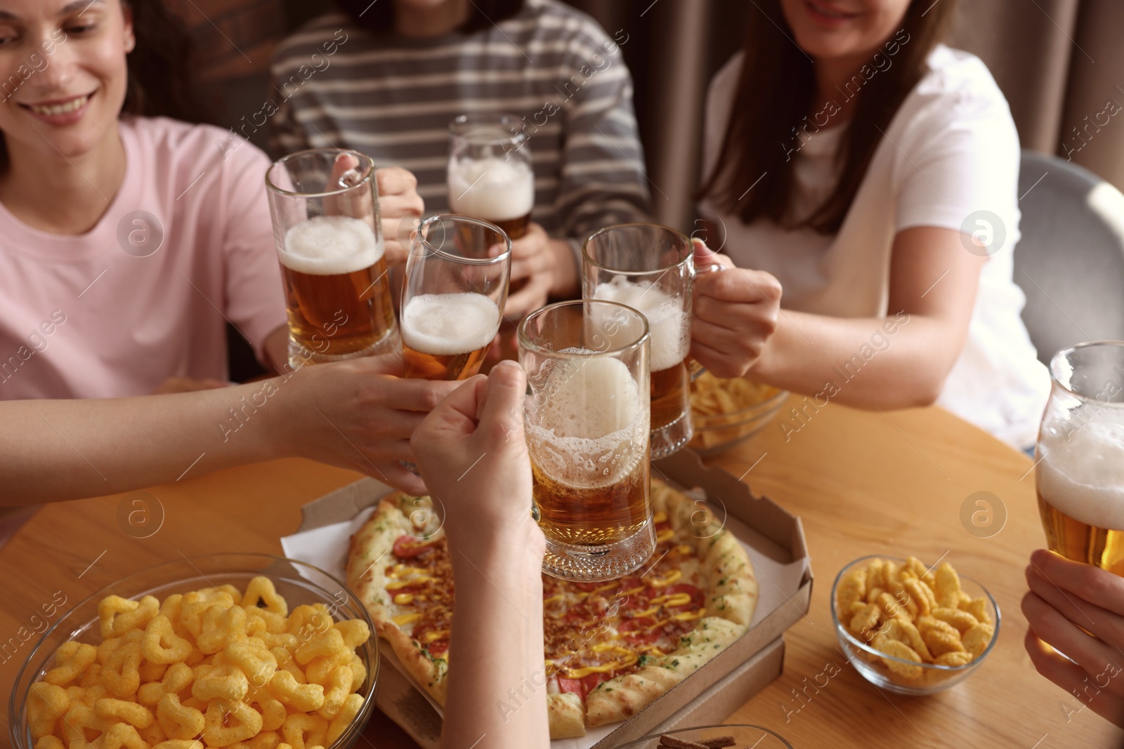 Photo of Group of happy friends clinking glasses of beer at table indoors, selective focus