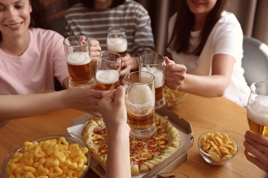 Photo of Group of happy friends clinking glasses of beer at table indoors, selective focus