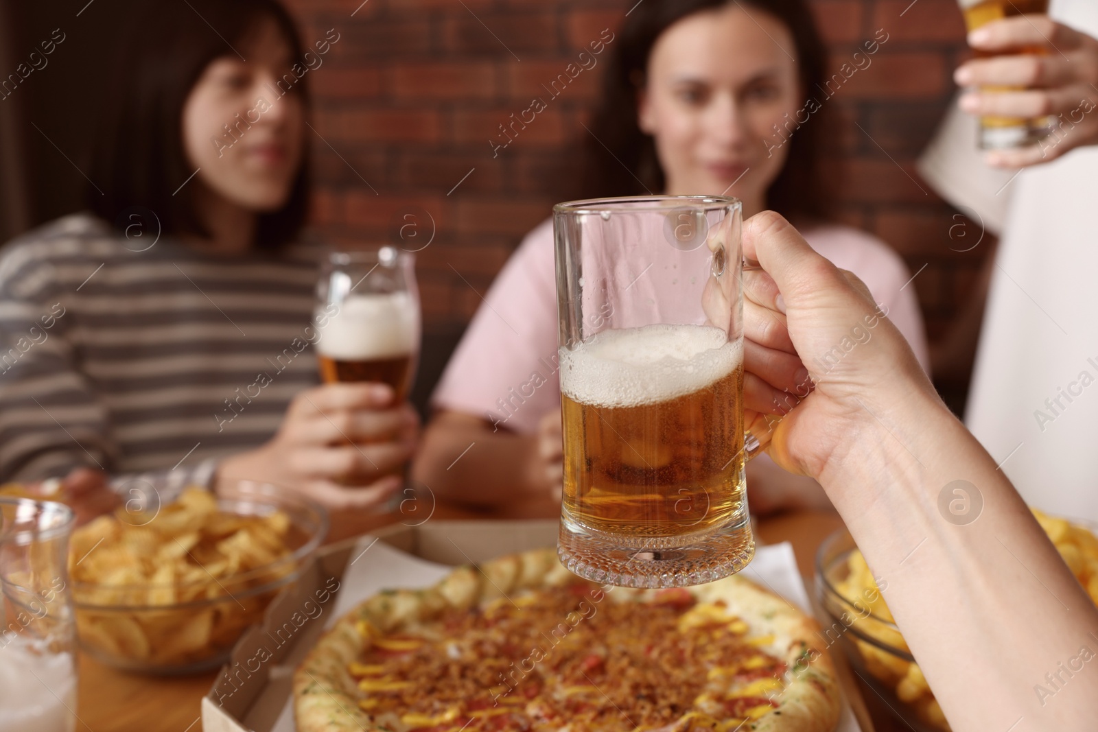 Photo of Group of happy friends clinking glasses of beer at table indoors, selective focus