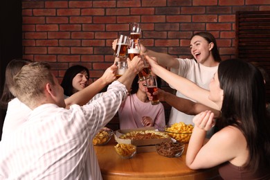 Photo of Group of happy friends clinking glasses of beer at table indoors
