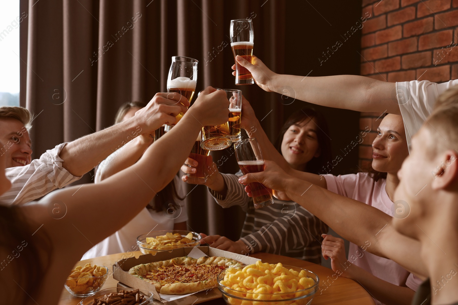 Photo of Group of happy friends clinking glasses of beer at table indoors, selective focus