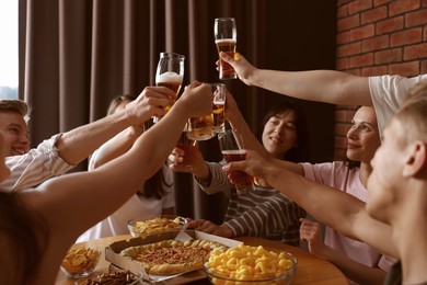 Photo of Group of happy friends clinking glasses of beer at table indoors, selective focus