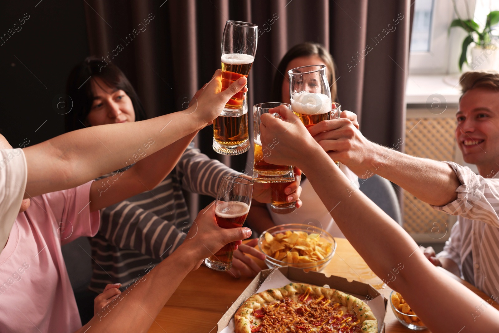 Photo of Group of happy friends clinking glasses of beer at table indoors, selective focus