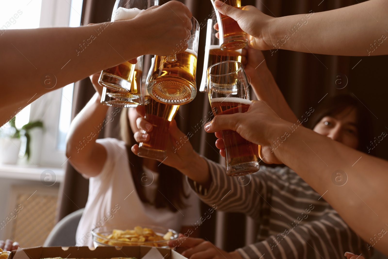 Photo of Group of happy friends clinking glasses of beer at table indoors, low angle view