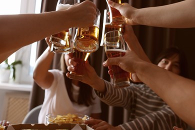 Photo of Group of happy friends clinking glasses of beer at table indoors, low angle view