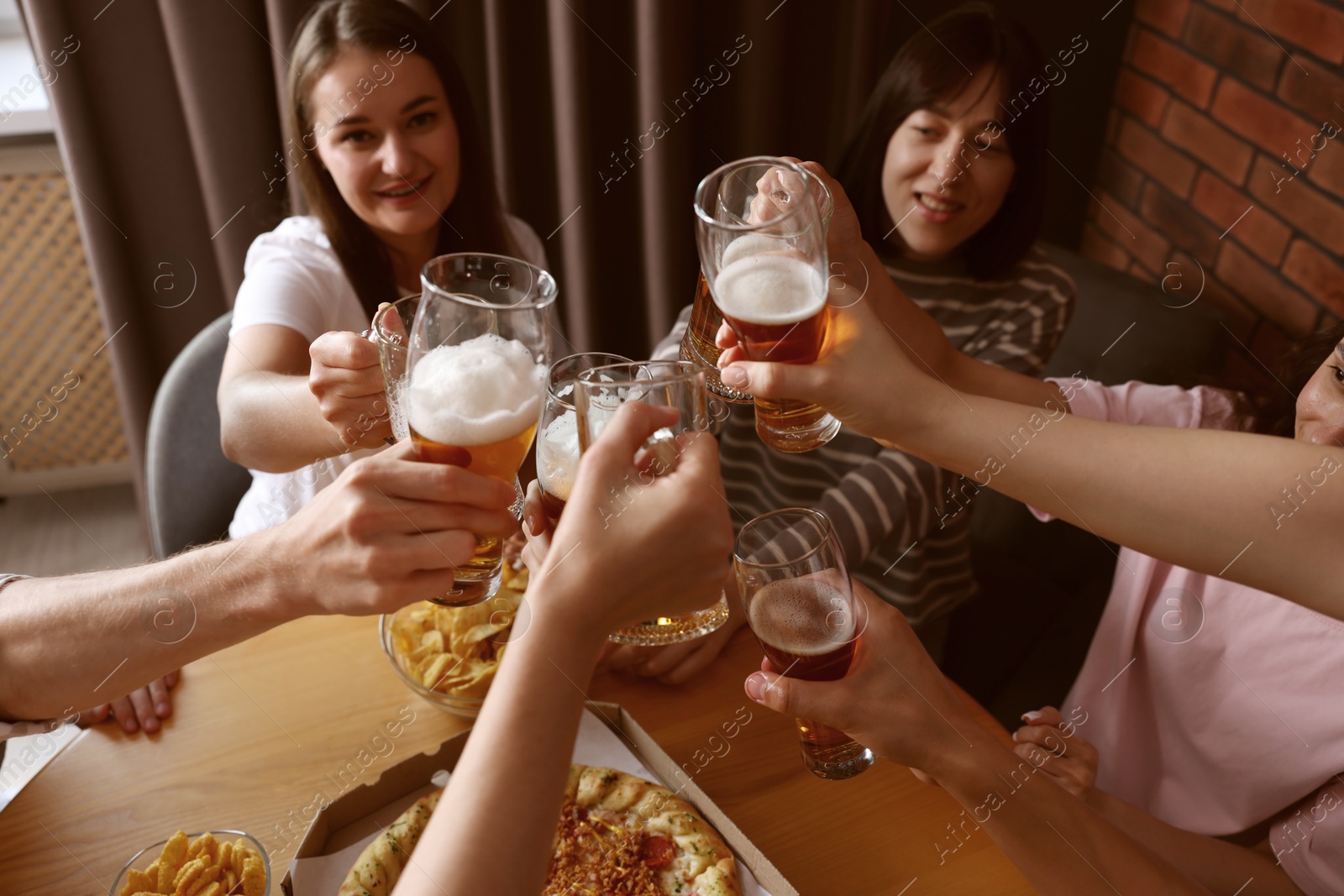 Photo of Group of happy friends clinking glasses of beer at table indoors, selective focus