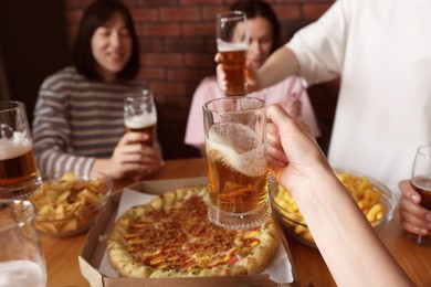 Photo of Group of happy friends clinking glasses of beer at table indoors, selective focus