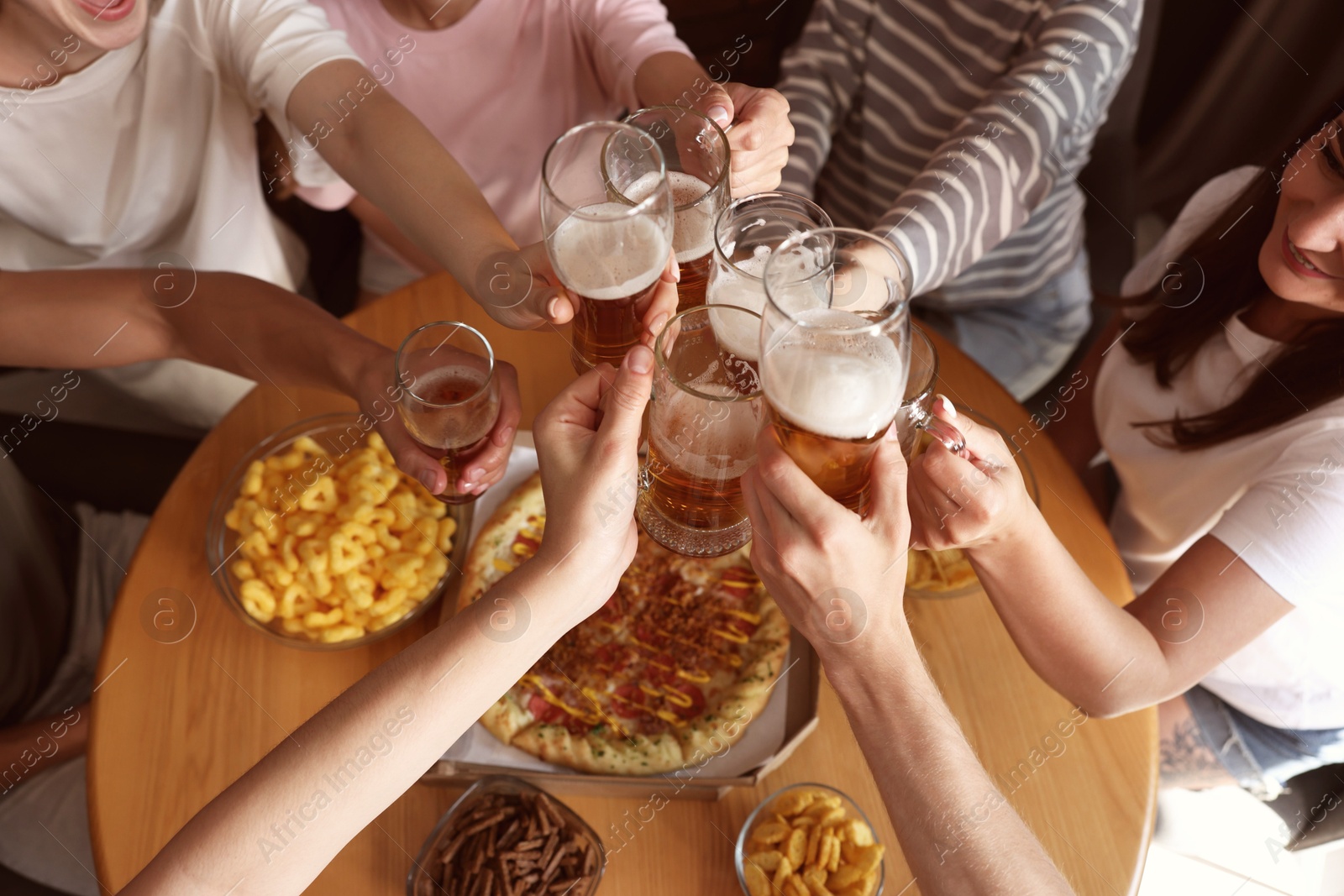 Photo of Group of happy friends clinking glasses of beer at table indoors, above view