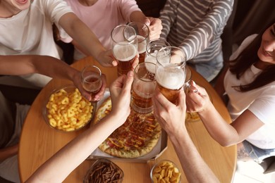 Photo of Group of happy friends clinking glasses of beer at table indoors, above view
